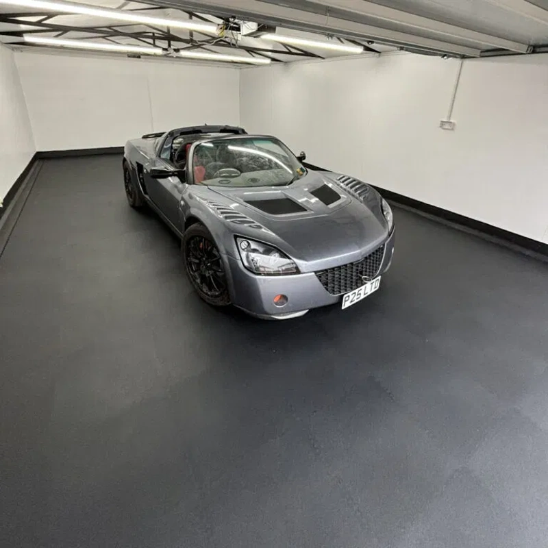 Silver sports car parked on smooth black garage flooring.