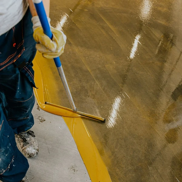 Worker applies yellow epoxy coating to a concrete floor with a squeegee.