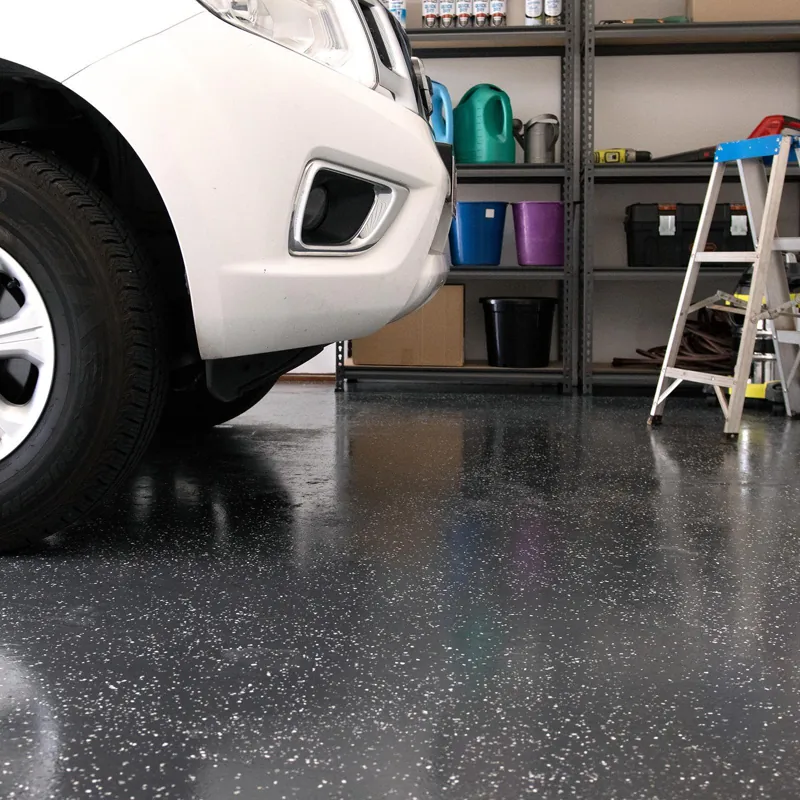 Close-up of a white car parked on a speckled dark gray epoxy garage floor.