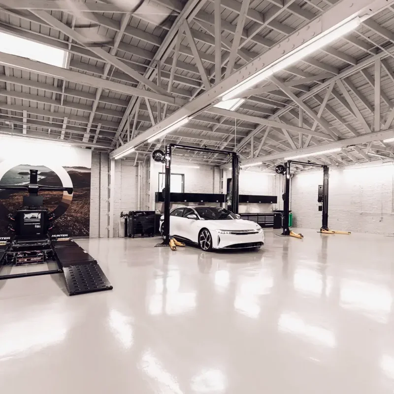 White Lucid Air electric car on a gleaming epoxy garage floor with lifts