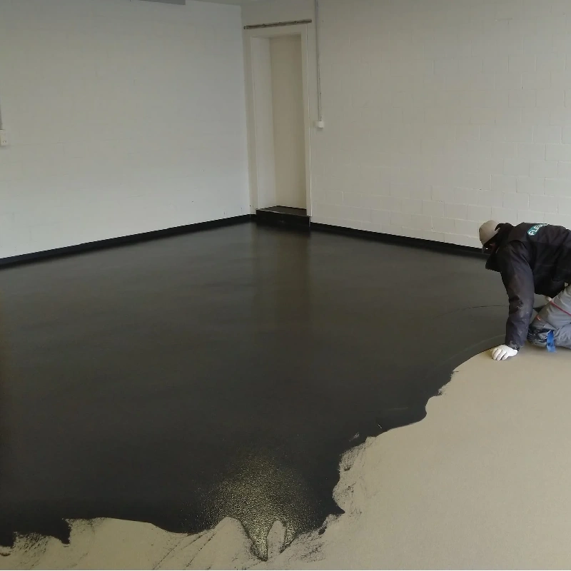 Worker applying dark grey epoxy floor coating in a garage