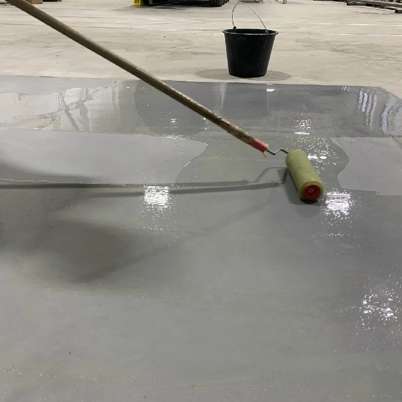 Applying a grey epoxy floor coating with a paint roller.